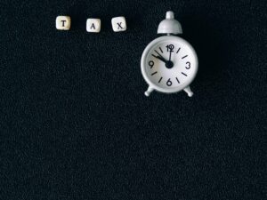 pexels-photo-6863256-6863256 Miniature clock and word tax on black background symbolizing tax season deadlines.