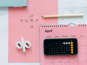 pexels-photo-6863515-6863515 Flat lay of April calendar with calculator, pencil, and pink background for financial planning.